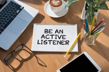 Notepad surrounded by office supplies that says "Be an Active Listener"